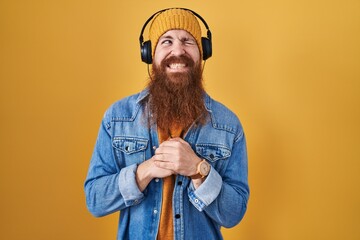 Canvas Print - Caucasian man with long beard listening to music using headphones laughing nervous and excited with hands on chin looking to the side