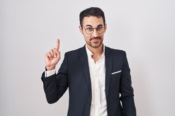 Sticker - Handsome business hispanic man standing over white background showing and pointing up with finger number one while smiling confident and happy.