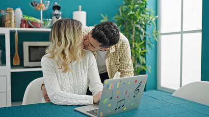 Wall Mural - Man and woman couple sitting on table using laptop kissing at dinning room