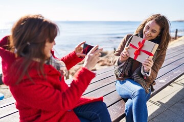 Poster - Two women mother and daughter make photo by smartphone holding gift at seaside