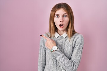 Canvas Print - Beautiful woman standing over pink background surprised pointing with finger to the side, open mouth amazed expression.