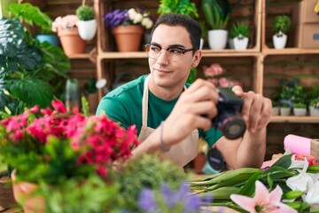 Sticker - Young hispanic man florist holding professional camera at flower shop