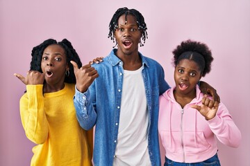 Canvas Print - Group of three young black people standing together over pink background surprised pointing with hand finger to the side, open mouth amazed expression.