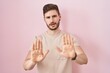 Hispanic man with beard standing over pink background moving away hands palms showing refusal and denial with afraid and disgusting expression. stop and forbidden.