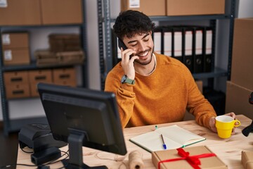 Poster - Young hispanic man ecommerce business worker talking on smartphone drinking coffee at office