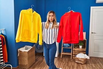 Canvas Print - Young blonde woman holding clean laundry on hangers depressed and worry for distress, crying angry and afraid. sad expression.