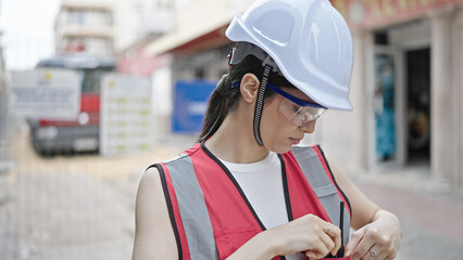 Wall Mural - Young beautiful hispanic woman builder standing with serious expression looking down at street