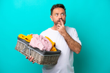 Wall Mural - Middle age woman holding a clothes basket isolated on blue background having doubts while looking up