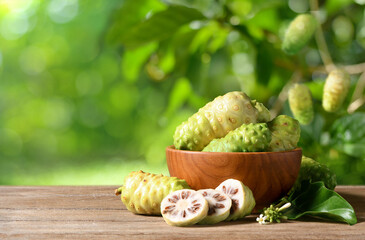 Noni or Morinda Citrifolia fruits on wooden table with blur plant background.