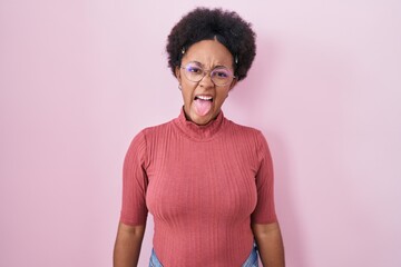 Poster - Beautiful african woman with curly hair standing over pink background sticking tongue out happy with funny expression. emotion concept.