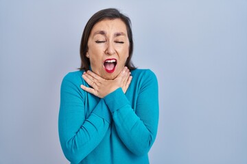 Wall Mural - Middle age hispanic woman standing over isolated background shouting and suffocate because painful strangle. health problem. asphyxiate and suicide concept.