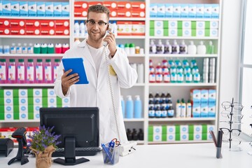 Canvas Print - Young caucasian man pharmacist talking on telephone using touchpad at pharmacy