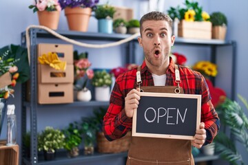 Canvas Print - Young caucasian man working at florist holding open sign afraid and shocked with surprise and amazed expression, fear and excited face.