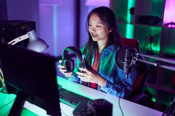 Canvas Print - Young chinese woman streamer using computer holding headphones at gaming room