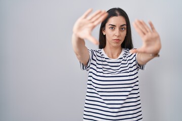 Sticker - Young brunette woman wearing striped t shirt doing frame using hands palms and fingers, camera perspective