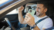 © Krakenimages.com - Young hispanic man using smartphone sitting on car with winner expression at street