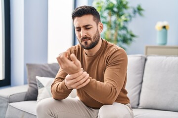 Sticker - Young hispanic man suffering for wrist injury sitting on sofa at home