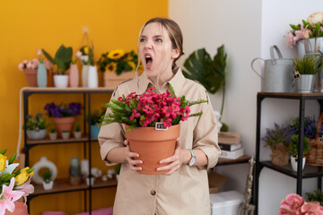 Wall Mural - Young caucasian woman working at florist shop holding plant pot angry and mad screaming frustrated and furious, shouting with anger. rage and aggressive concept.