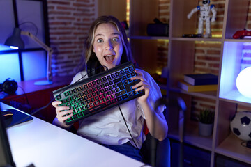 Poster - Young caucasian woman holding gamer keyboard celebrating crazy and amazed for success with open eyes screaming excited.