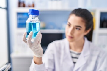 Young beautiful hispanic woman scientist holding bottle at laboratory