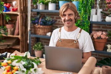 Poster - Young blond man florist smiling confident using laptop at flower shop