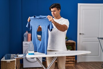 Canvas Print - Hispanic man ironing holding burned iron shirt at laundry room skeptic and nervous, frowning upset because of problem. negative person.