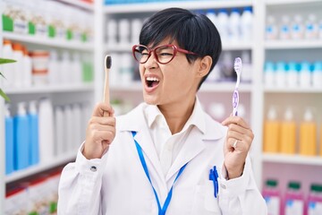 Poster - Young asian woman with short hair doing toothbrush comparative at pharmacy angry and mad screaming frustrated and furious, shouting with anger. rage and aggressive concept.