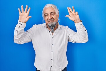 Wall Mural - Middle age man with grey hair standing over blue background showing and pointing up with fingers number nine while smiling confident and happy.