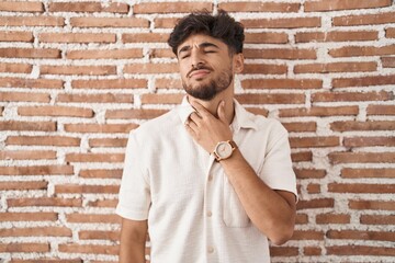 Poster - Arab man with beard standing over bricks wall background touching painful neck, sore throat for flu, clod and infection