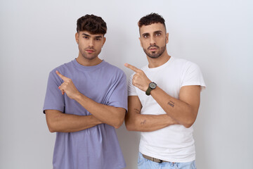 Canvas Print - Homosexual gay couple standing over white background pointing with hand finger to the side showing advertisement, serious and calm face