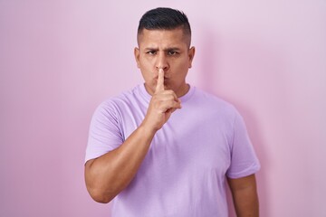 Canvas Print - Young hispanic man standing over pink background asking to be quiet with finger on lips. silence and secret concept.