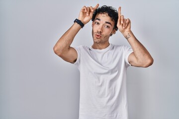 Poster - Hispanic man standing over isolated background doing funny gesture with finger over head as bull horns