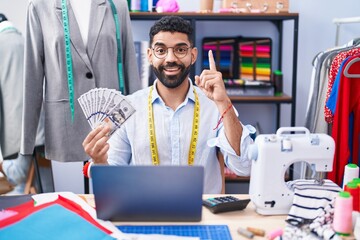 Poster - Hispanic man with beard dressmaker designer holding dollars surprised with an idea or question pointing finger with happy face, number one