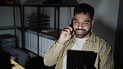 Poster - Young hispanic man business worker talking on smartphone using touchpad at office