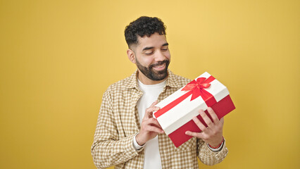 Sticker - Young hispanic man smiling confident holding gift over isolated yellow background