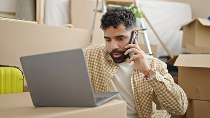 Canvas Print - Young hispanic man using laptop talking on smartphone at new home