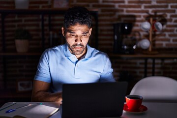 Wall Mural - Hispanic man with beard using laptop at night depressed and worry for distress, crying angry and afraid. sad expression.