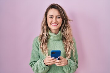 Wall Mural - Young caucasian woman using smartphone typing message smiling with a happy and cool smile on face. showing teeth.