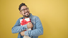 Young Latin Man Smiling Confident Hugging Gift Over Isolated Yellow Background