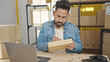 © Krakenimages.com - Young latin man ecommerce business worker using laptop writing on package at office