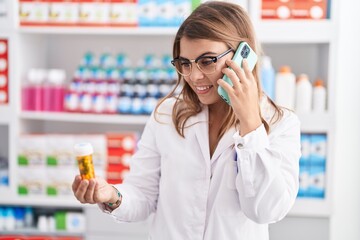 Wall Mural - Young woman pharmacist holding pills bottle talking on smartphone at pharmacy