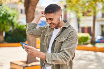 Wall Mural - Young hispanic man smiling confident playing video game at park