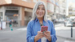 © Krakenimages.com - Middle age grey-haired woman using smartphone smiling at street