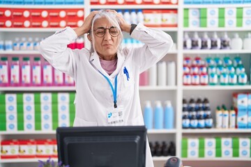 Wall Mural - Middle age woman with tattoos working at pharmacy drugstore suffering from headache desperate and stressed because pain and migraine. hands on head.