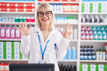 Wall Mural - Young caucasian woman working at pharmacy drugstore showing and pointing up with fingers number eight while smiling confident and happy.