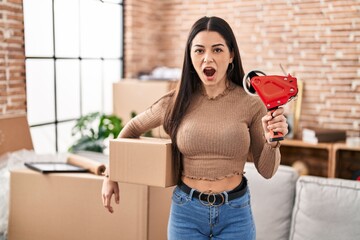 Poster - Young woman moving to a new home packing boxes afraid and shocked with surprise and amazed expression, fear and excited face.