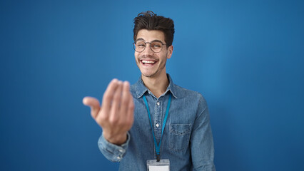 Wall Mural - Young hispanic man smiling confident doing come gesture with hands over isolated blue background