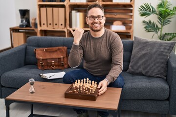 Sticker - Middle age caucasian man playing chess sitting on the sofa pointing thumb up to the side smiling happy with open mouth