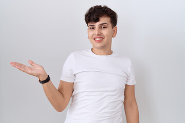 Canvas Print - Young non binary man wearing casual white t shirt smiling cheerful presenting and pointing with palm of hand looking at the camera.