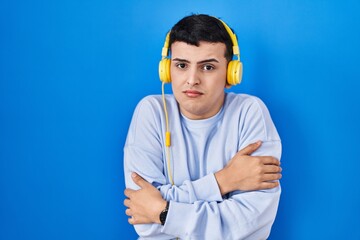 Sticker - Non binary person listening to music using headphones shaking and freezing for winter cold with sad and shock expression on face